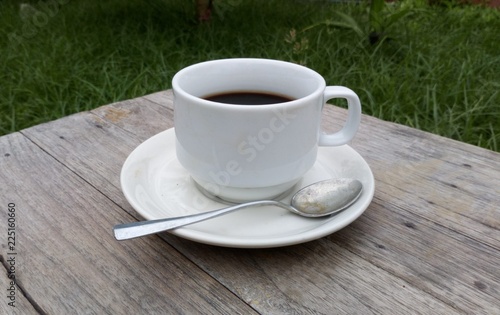Black coffee in white glass placed on an old wooden table in a green garden.In the morning light sunshine.
