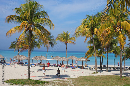 Tropical beach with sand and palms on seashore and people playing volleyball