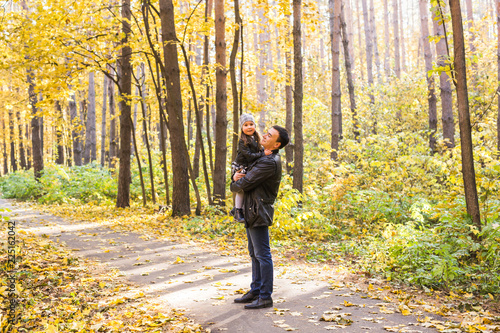 Fatherhood, family and leisure concept - father holding little daughter in his arms in autumn park
