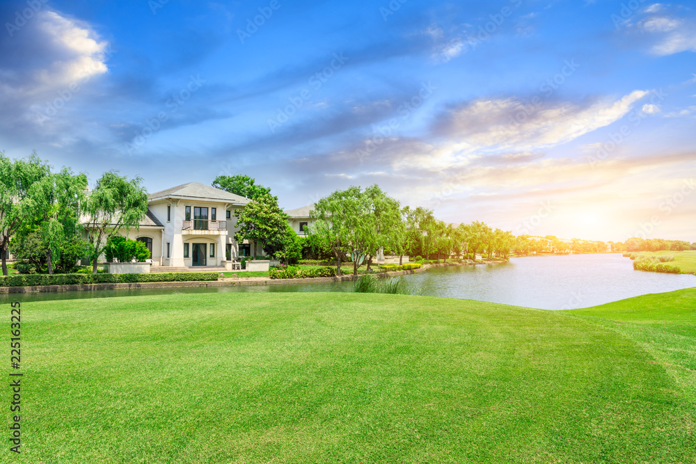 Obraz premium Green meadow and woods with apartment buildings scenery at sunset