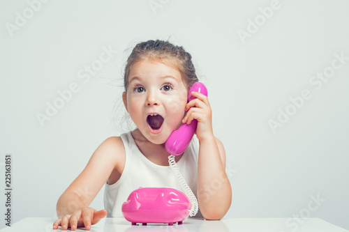 beautiful cute little girl talking on toy telephone with very excited expression photo