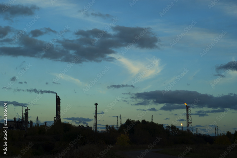 silhouette industrial landscape with industrial torches and fractionating columns against the background of a dark evening sky