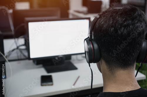 Education e-learning foreign languages Concept : Asian Student Young man wearing Headphones listening English songs music and searching for learning abroad in computer pc at classroom of university