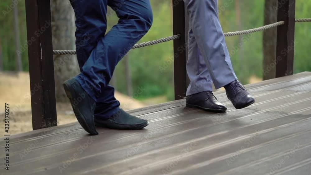 Two man staying on patio or terrace and talking. Weared in suit and classic shoes. Outdoors in summer, legs closeup. Two man staying on patio or terrace and talking. Weared in suit and classic shoes. Outdoors in summer, legs closeup.
