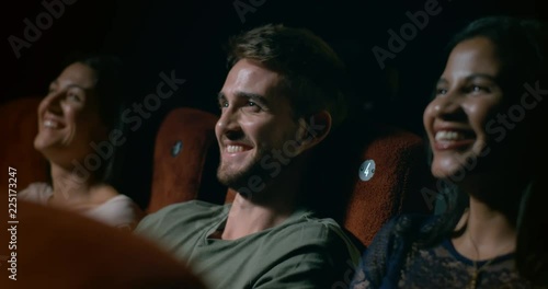 Young man sitting with his friends in a movie theatre laughing and having fun. Slow motion.