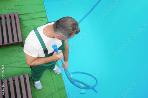 Male worker cleaning outdoor pool with underwater vacuum, above view
