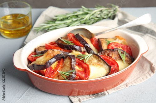 Baked eggplant with tomatoes, cheese and rosemary in dishware on table