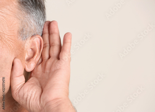 Mature man with hearing problem on light background, closeup. Space for text