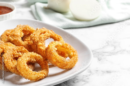 Plate with homemade crunchy fried onion rings on marble table, closeup. Space for text