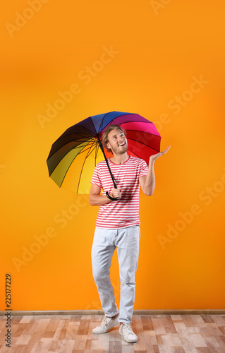 Man with rainbow umbrella near color wall