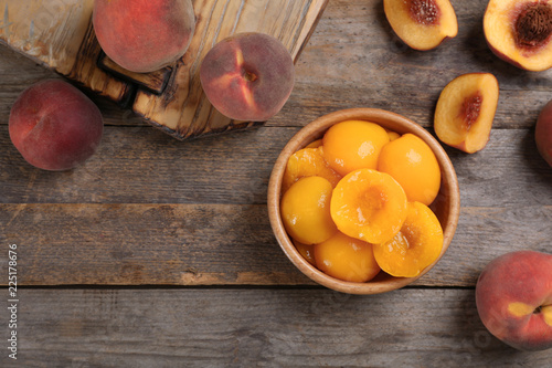 Flat lay composition with canned and fresh peaches on wooden background. Space for text