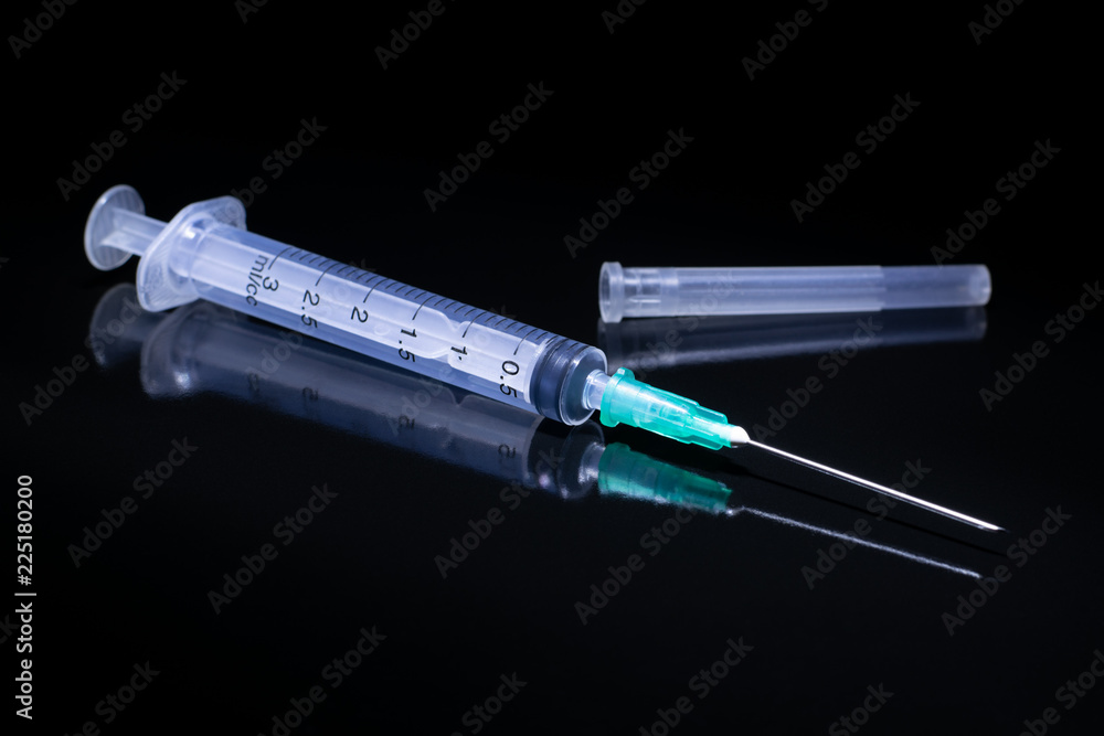 A medical syringe lying on a black reflective surface. A medical syringe lying on a black reflective surface.