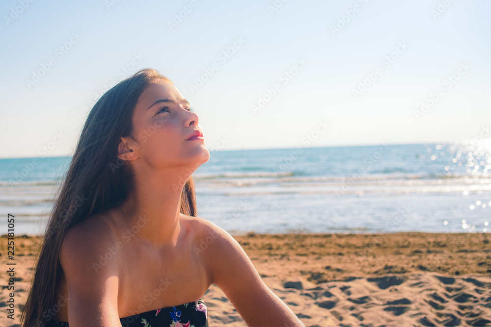 young model girl sits on the sand by the sea, looks into the distance thoughtfully and seriously