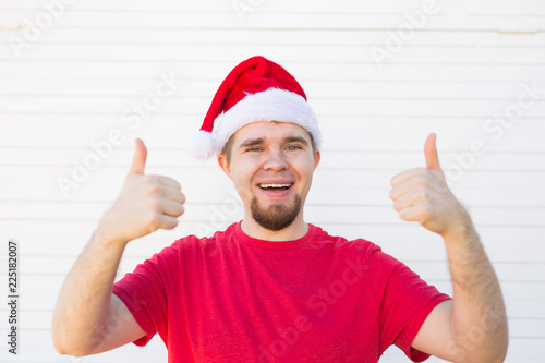 Young man with a christmas hat making a thumb up sign on white background © satura_
