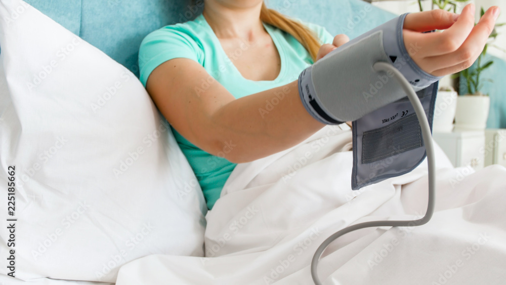 Closeup image of woman lying in bed and wearing digital blood pressure manometer sleeve on hand Closeup image of woman lying in bed and wearing digital blood pressure manometer sleeve on hand