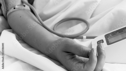 Black and white closeup image of female hand measuring blood pressure with digital manometer