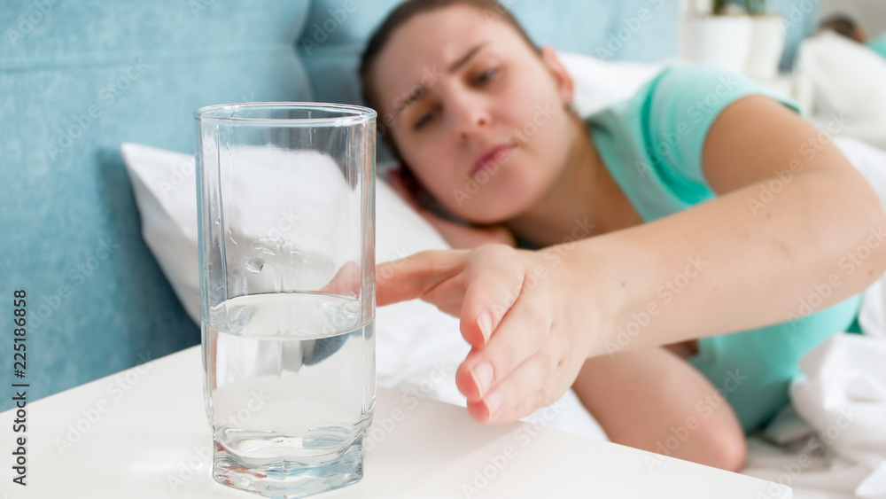Portrait of sick woman taking glass of water from bedside table Portrait of sick woman taking glass of water from bedside table
