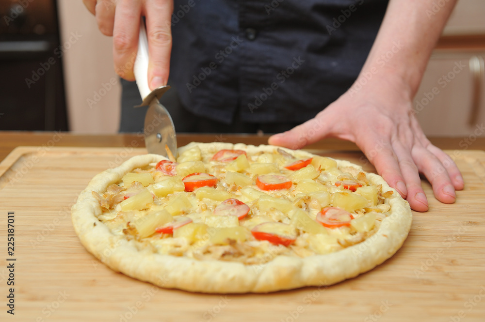The man cuts the cooked pizza on the table in the kitchen, hands close up
