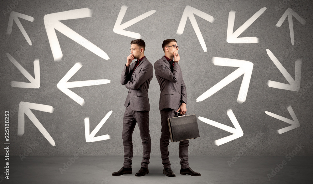 © ra2 studio - Young conflicted businessman choosing between two directions with arrows around him