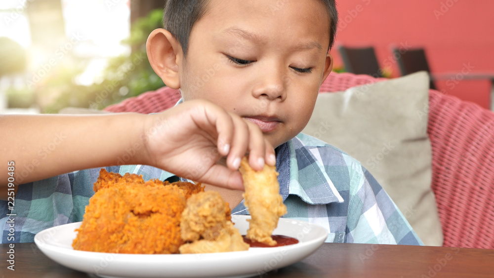 Cute asian boy are happy eating fried chicken leg in restaurant Cute asian boy are happy eating fried chicken leg in restaurant