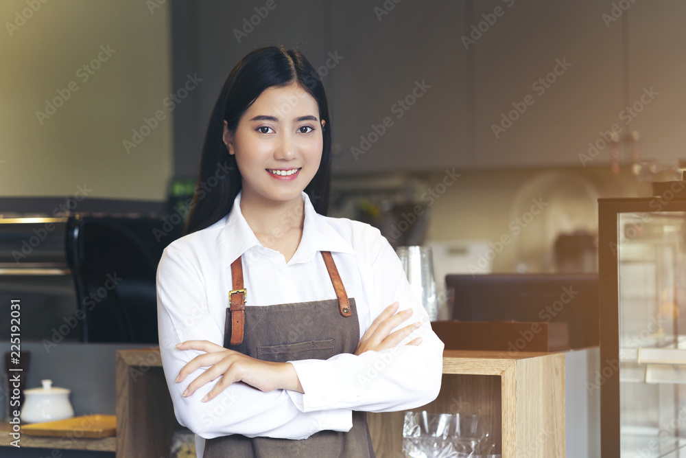 Portrait of young woman barista with brown apron uniform. Standing with arm cross pose, look professional of entrepreneur, beautiful female SME business ownership Portrait of young woman barista with brown apron uniform. Standing with arm cross pose, look professional of entrepreneur, beautiful female SME business ownership