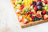 Healthy raw fruits and berries platter, strawberries raspberries oranges plums apples kiwis grapes blueberries, mango on the serving board, top view, copy space, selective focus