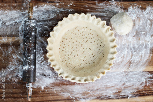 Εκτύπωση καμβά Homemade butter pie crust in pie plate with fluted pinched edge, rolling pin and extra ball of dough over floured rustic wooden background