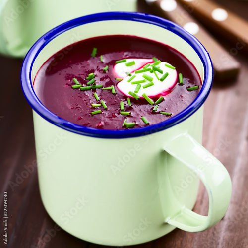 Fresh homemade beetroot cream soup in enamel cup, garnished with cream and chives (Selective Focus, Focus one third into the soup)