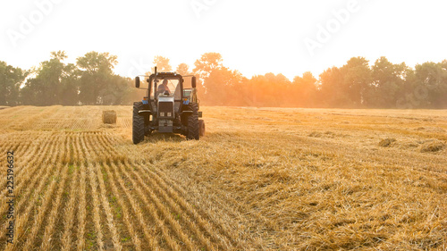 Tractor with farmer on the field. Front view. Making hay bales. photo
