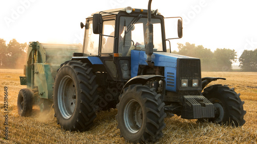 Blue tractor and trail on the field. Making big round bales of hay.