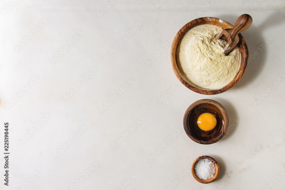 Ingredients for homemade italian pasta ravioli cooking semolina flour, egg yolk, sea salt in olive wood bowls over white marble background. Flat lay, space. Home baking concept