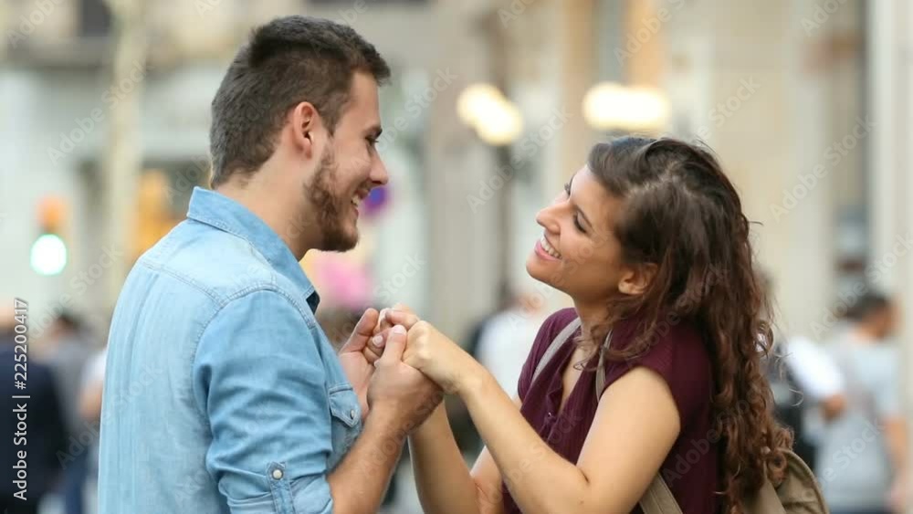 Side view of a happy couple flirting holding hands and hugging in the street Side view of a happy couple flirting holding hands and hugging in the street