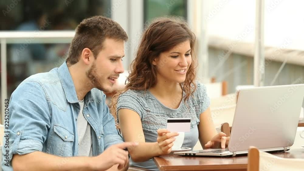 Happy couple shopping online with a credit card and a laptop in a coffee shop Happy couple shopping online with a credit card and a laptop in a coffee shop