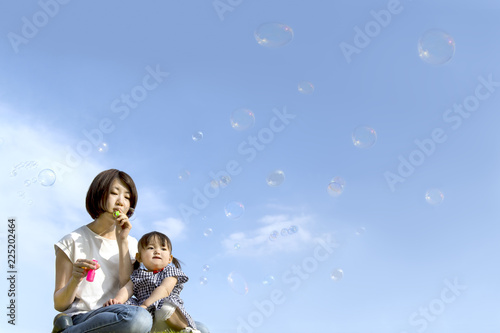 公園で青空バックにシャボン玉をして遊ぶ幸せな親子。家族、親子、幸せ、愛情、育児、健康イメージ © chikala