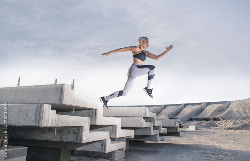 Middle Eastern Girl with short braided hair jumping of a stack of blocks on a construction site wearing gray and black fitness outfit on a hot bright sunny day. Middle Eastern Girl with short braided hair jumping of a stack of blocks on a construction site wearing gray and black fitness outfit on a hot bright sunny day.
