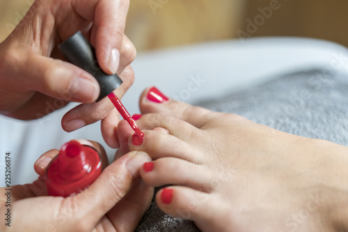 The master covers the customer's nails with varnish. Hands in gloves cares about a woman's foot nails. Pedicure, manicure beauty salon concept. Nail varnishing in red color.