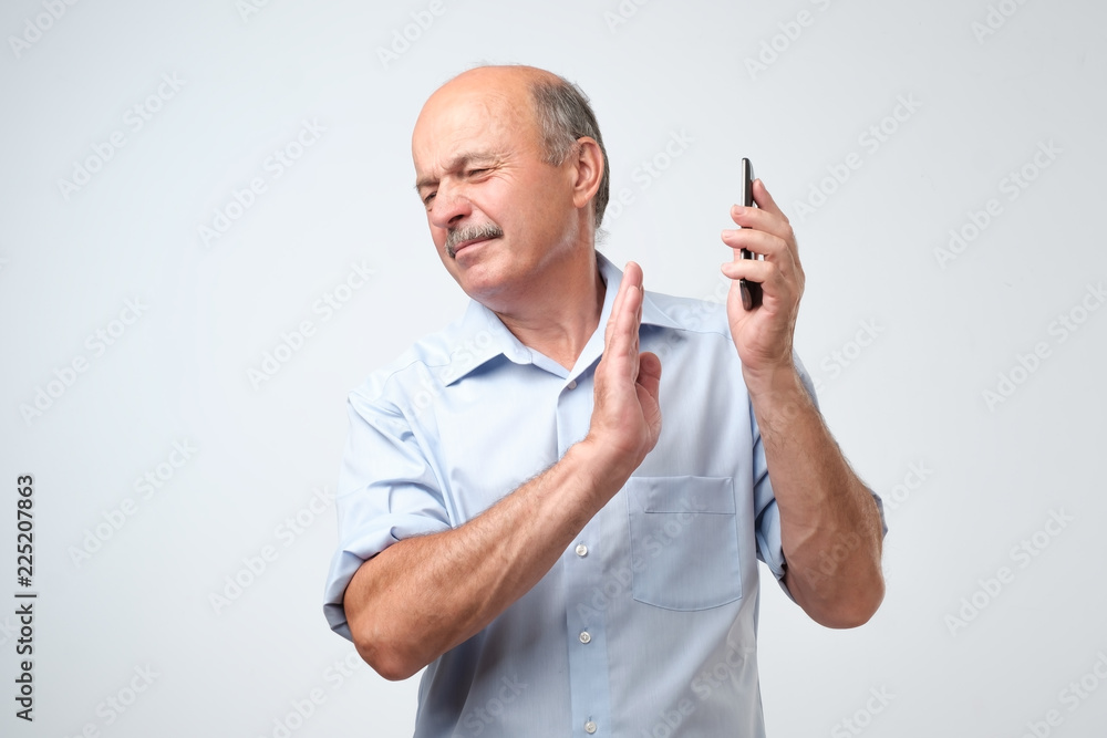 Mature handsome man refusing to speak on the phone over isolated background turning his face from it. Stop talking to me please. Mature handsome man refusing to speak on the phone over isolated background turning his face from it. Stop talking to me please.