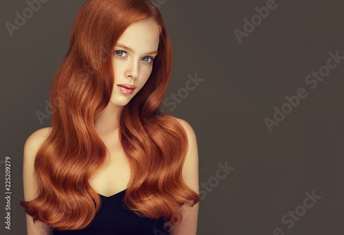 Red head girl with long  and   shiny curly hair .  Beautiful  model woman  with wavy  hairstyle. Care , cosmetic and beauty products
 photo