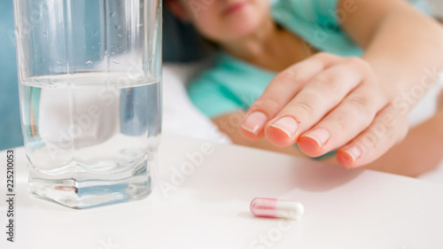 Closeup image of female hand reaching for pill lying on bedside table