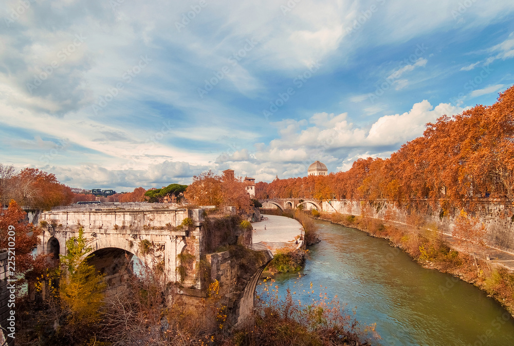 Autumn and foliage in Rome. Red and yellow leaves near Tiber Island with two ancient bridges, in the city historic center