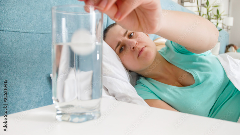 Portrait of young woman feeling unwell throwing pill in glass of water Portrait of young woman feeling unwell throwing pill in glass of water