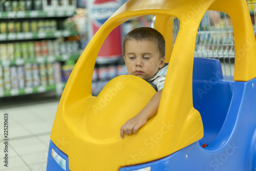 Kid is bored in the store. Sleeping boy is in the chair on the trolley in the supermarket.