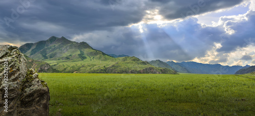 Sunbeams shining through the clouds over mountain ranges and valley - panoramic view