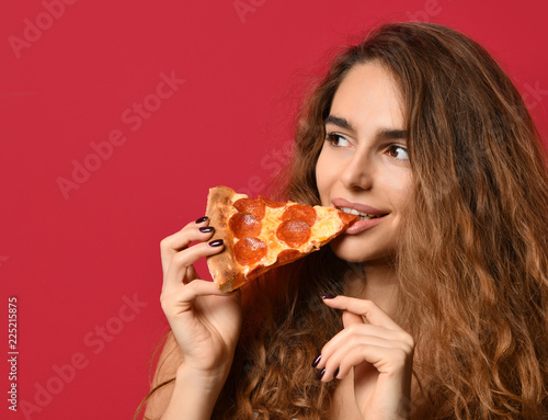 Young beautiful woman eat slice of pepperoni pizza with closed eyes smiling on red pink