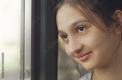 A young beautiful girl looks out the window and smiles. Close-up portrait.