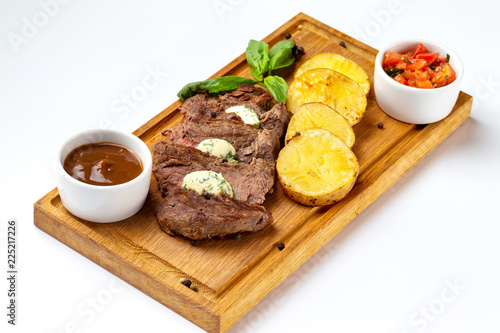 Wooden board with roast beef meat served with fried potatoes and tomato sauce isolated at white background.