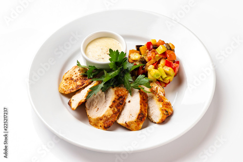 Plate with fried chicken breast served with ratatouille vegetables and sauce isolated at white background.