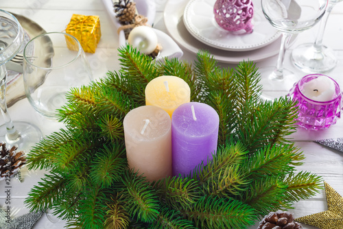 Festive decoration on Christmas table setting with candles, lantern, tableware and wine glasses on white wooden background