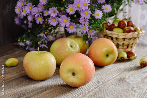 Ripe ruddy apples on a wooden table next to a bouquet of flowers