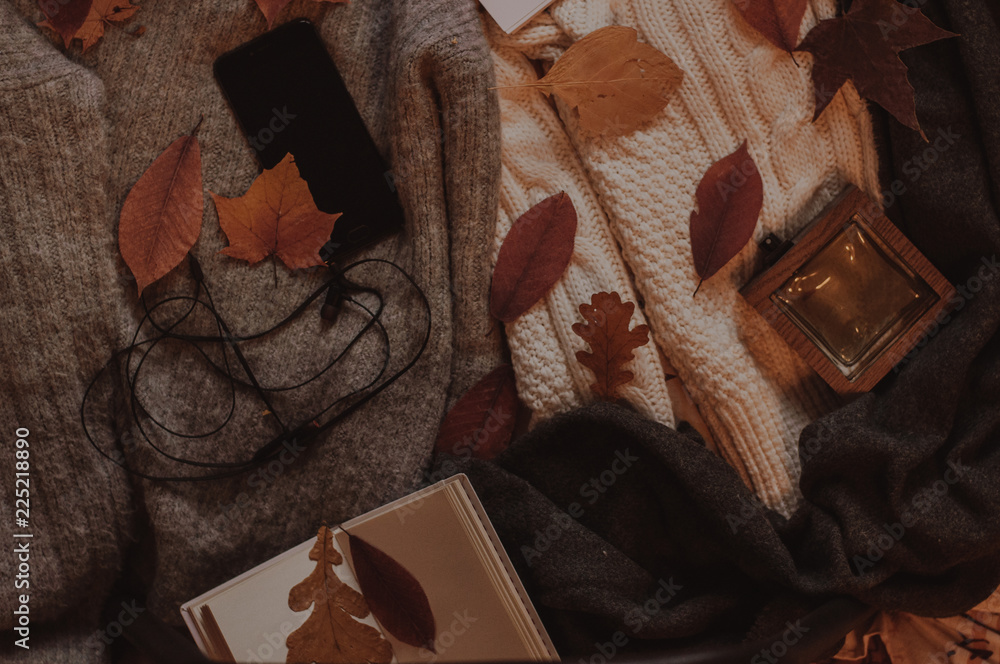 Fototapeta premium Autumn cozy flatlay. Smartphone with headphones, whiite ntebook and perfume on the autumn sweaters with scarf